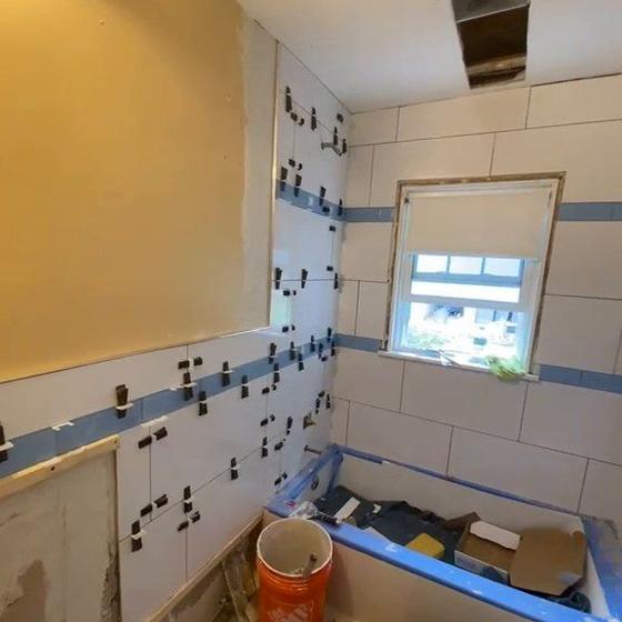 Bathroom wall tile going up around a window, levelling clips and blue tape still in place
