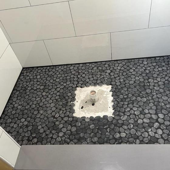 Black pebble mosaic shower floor around a centre drain